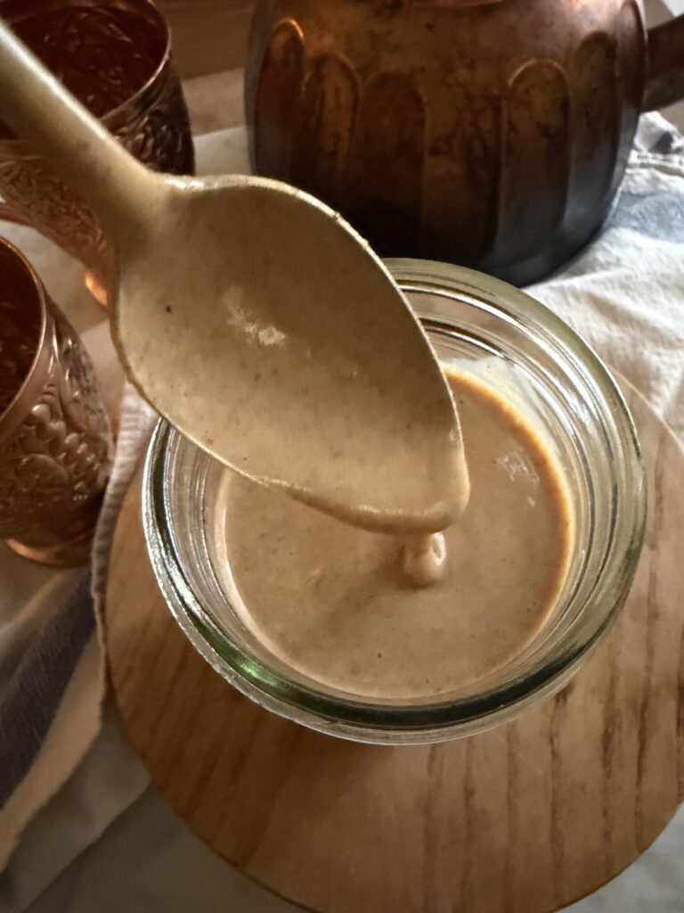 A spoonful of homemade fall pumpkin sauce is dripping into a glass mason jar