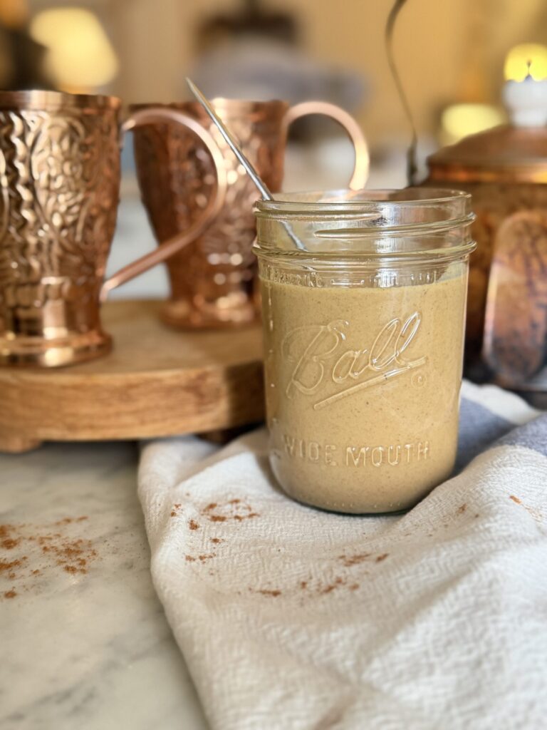 A jar of homemade pumpkin sauce for fall on a marble surface with copper cups and an antique tea kettle
