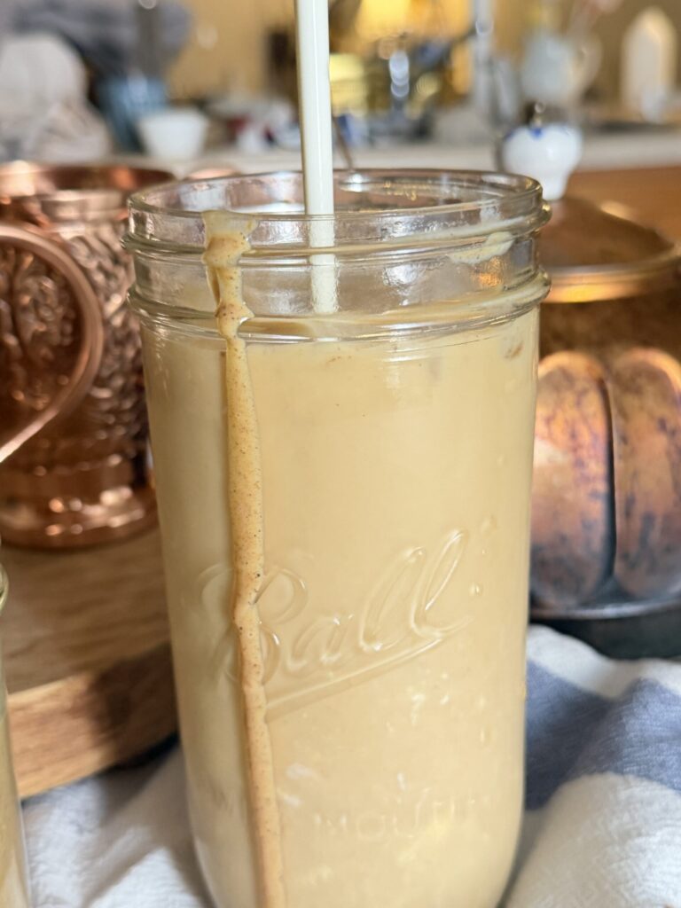 A tall glass of iced pumpkin chai tea with homemade pumpkin sauce with copper accents in the background