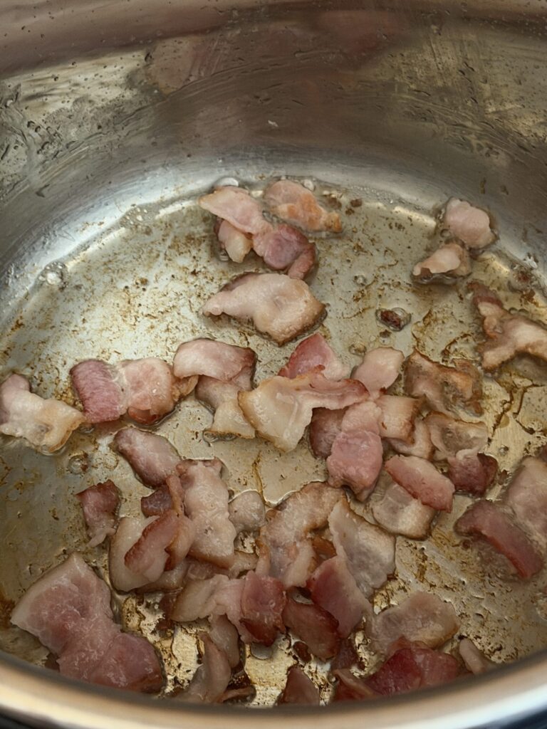 Chunks of cut bacon simmering in the bottom of a stainless  steel pot
