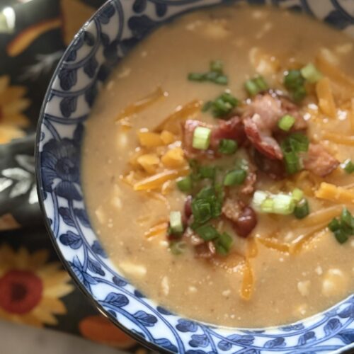 A bowl of creamy beer cheese soup with bacon, cheese, and scallions of a fall themed tea towel