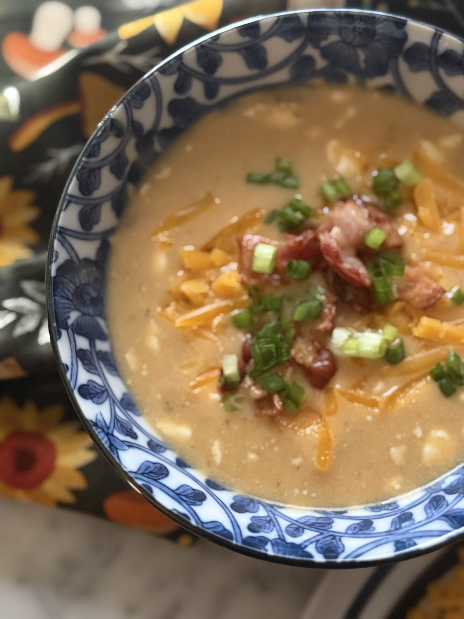 A bowl of creamy beer cheese soup with bacon, cheese, and scallions of a fall themed tea towel