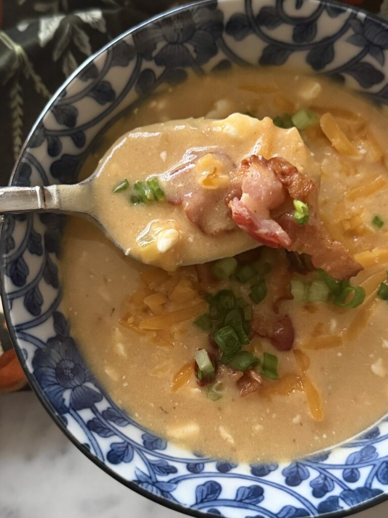 A spoonful of warm and comforting beer cheese soup with bacon in a blue and white bowl