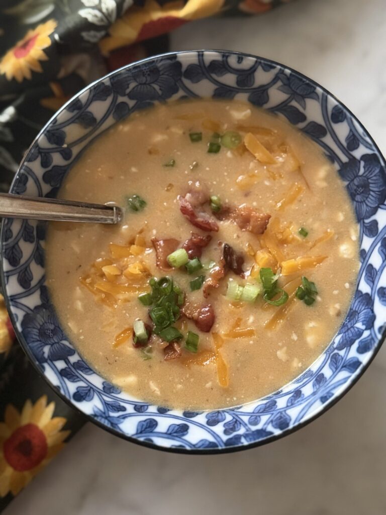 A blue bowl of creamy beer cheese soup with melted cheddar, crumbled bacon, and sliced scallions