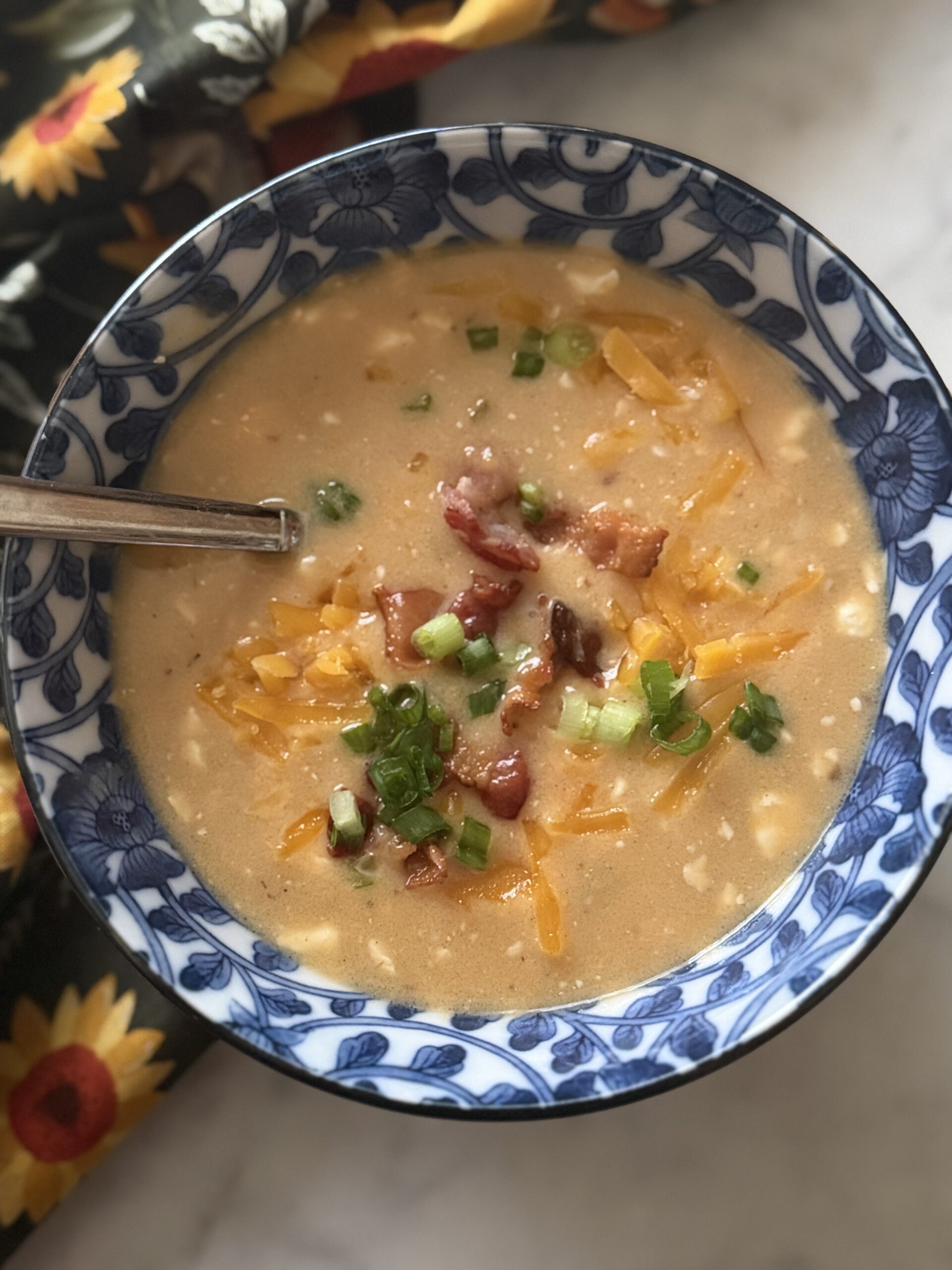 A blue bowl of creamy beer cheese soup with melted cheddar, crumbled bacon, and sliced scallions