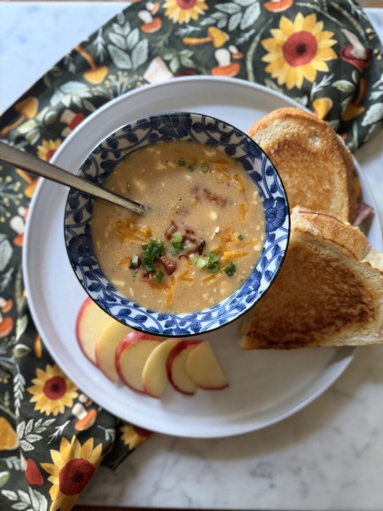 Creamy beer cheese soup is paired with sliced apples and a ham, cheddar, and apple panini