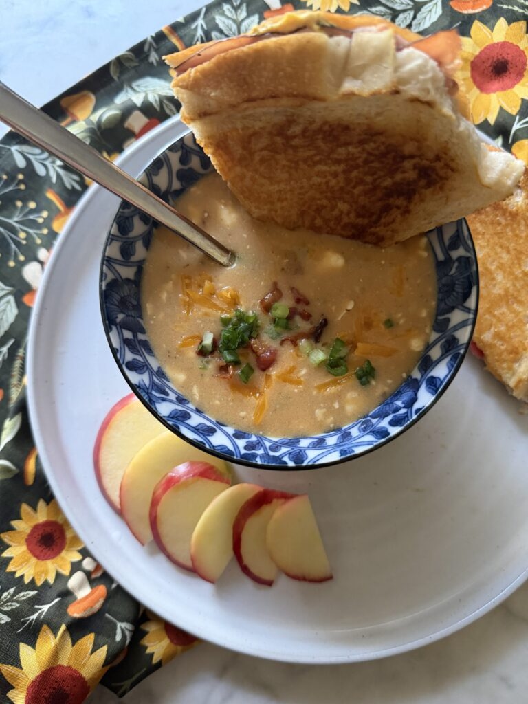 A warm panini is dipped in a savory bowl of beer cheese soup