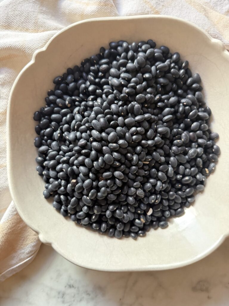 A large bowl of raw black beans on a marble surface