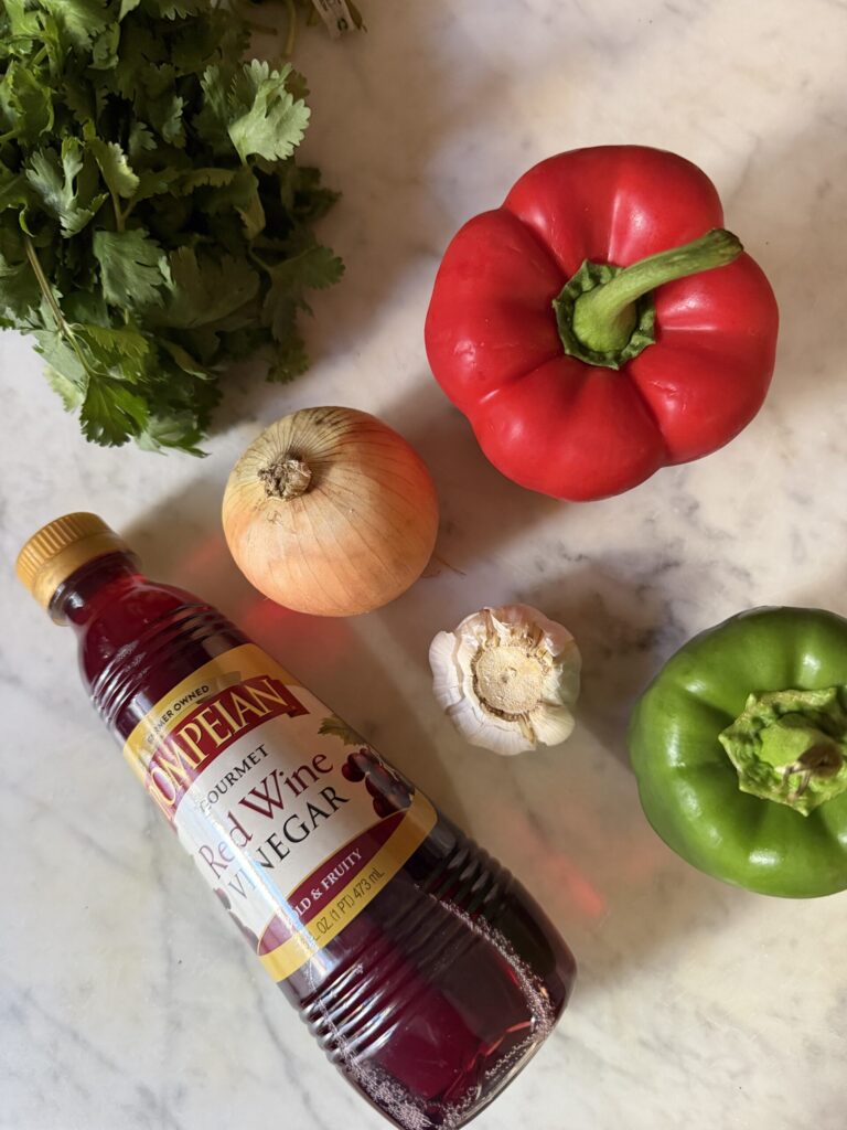 Fresh red and green bell peppers, onion, garlic, cilantro and red wine vinegar on a marble surface