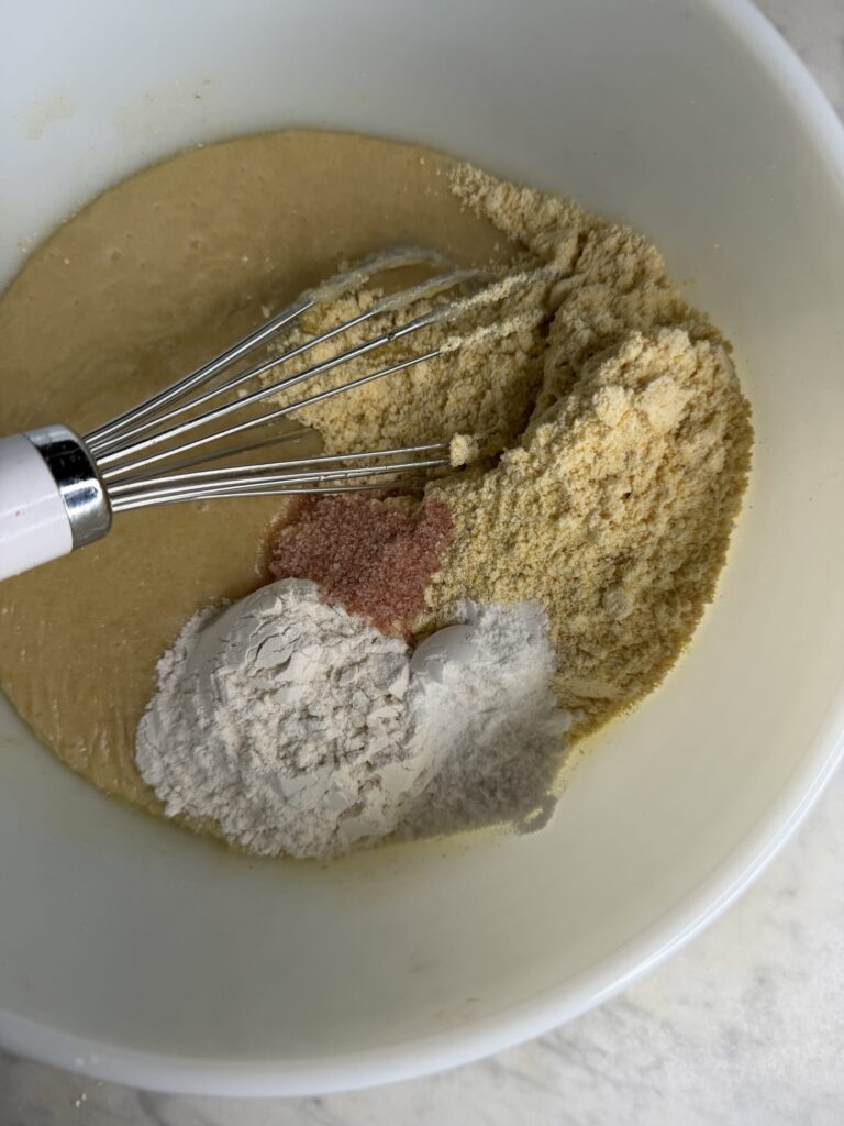 Dry ingredients for sourdough cornbread are added into the bowl of wet batter