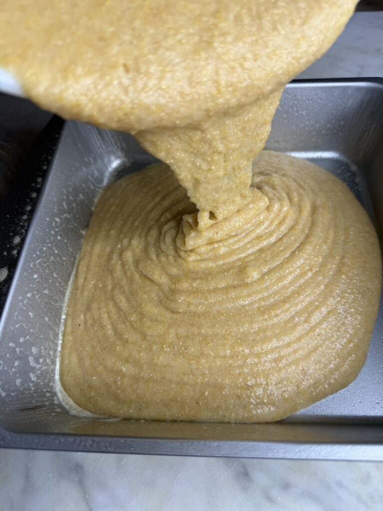 Sourdough cornbread batter is poured into a small square baking pan