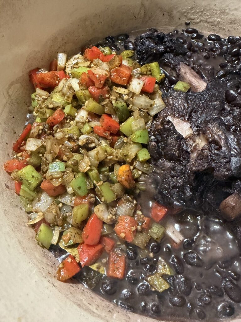 Sofrito is added to a pot of black beans and smoked ham hock to make soup
