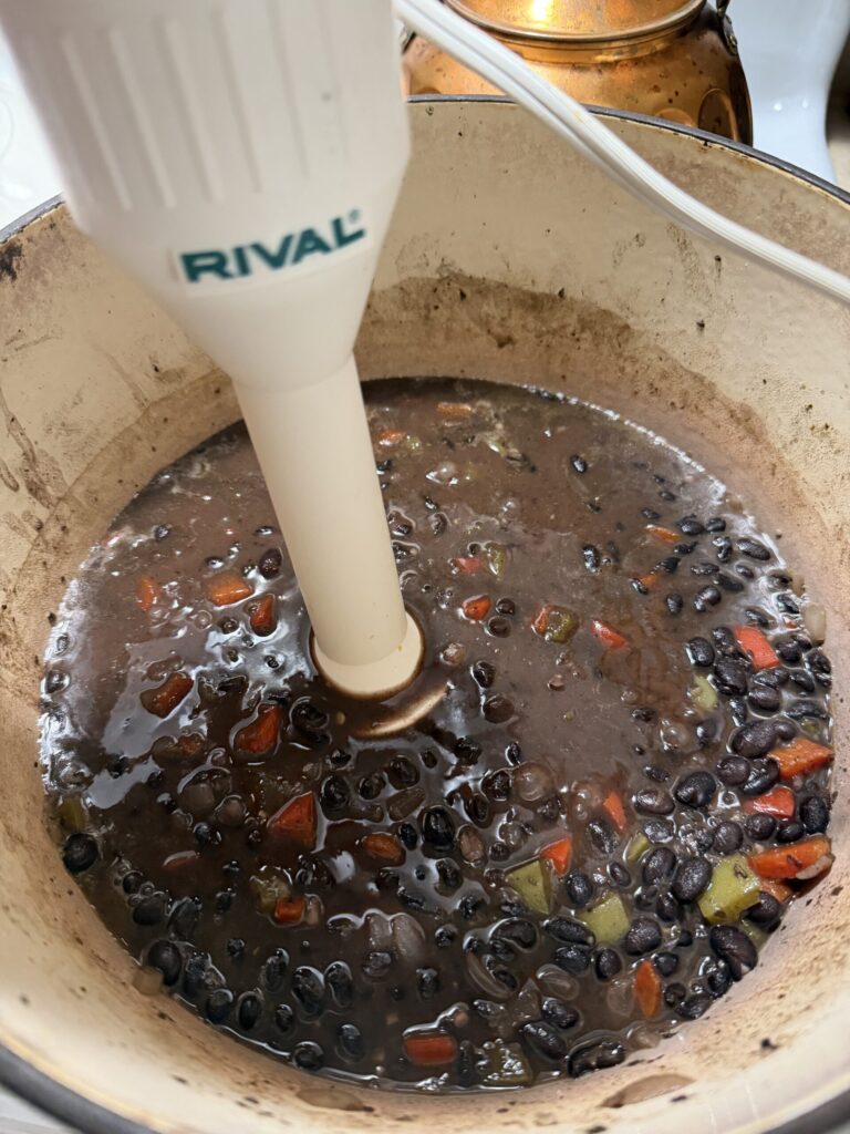 An immersion blender in a pot blending black bean soup