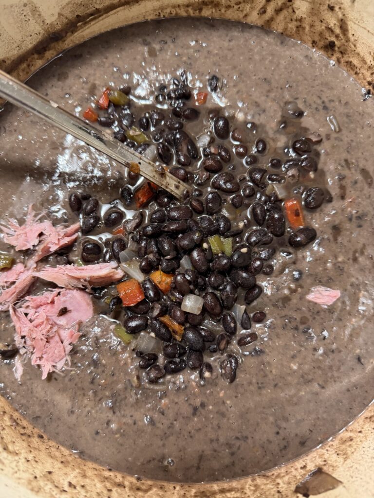 Smoked ham hock is shredded and put in a pot of black bean soup